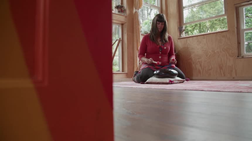 A woman is playing a small drum by the window