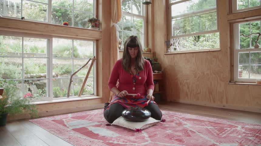 A woman is playing a meditation drum in a living room during the day