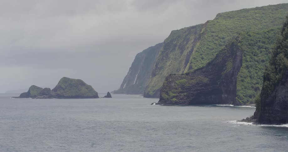 Waterfalls are cascading down cliffs into the ocean on a cloudy day