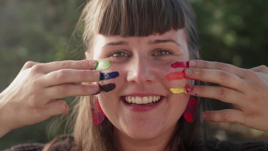 A woman paints her cheeks with paint from her fingertips