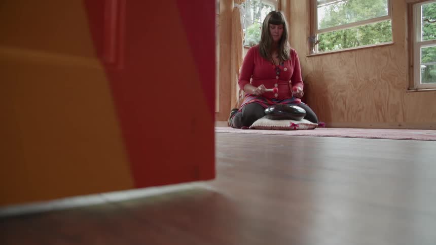 A woman plays a steel drum on the floor