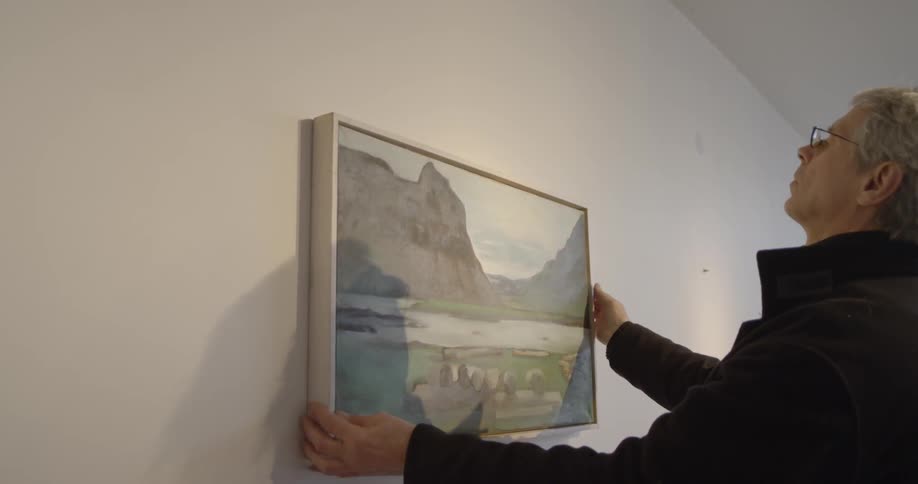 A person hangs a framed painting on a wall
