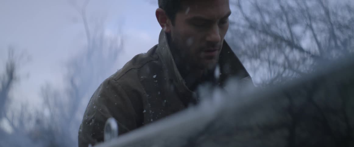 A man is lifting a bag from a pickup truck bed outside as it snows