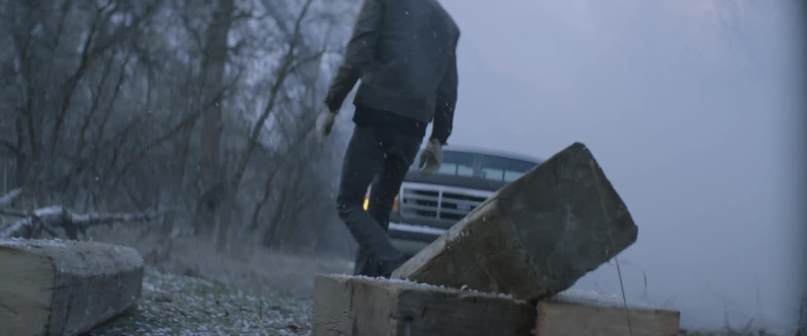 A man is carrying a large log in the snow