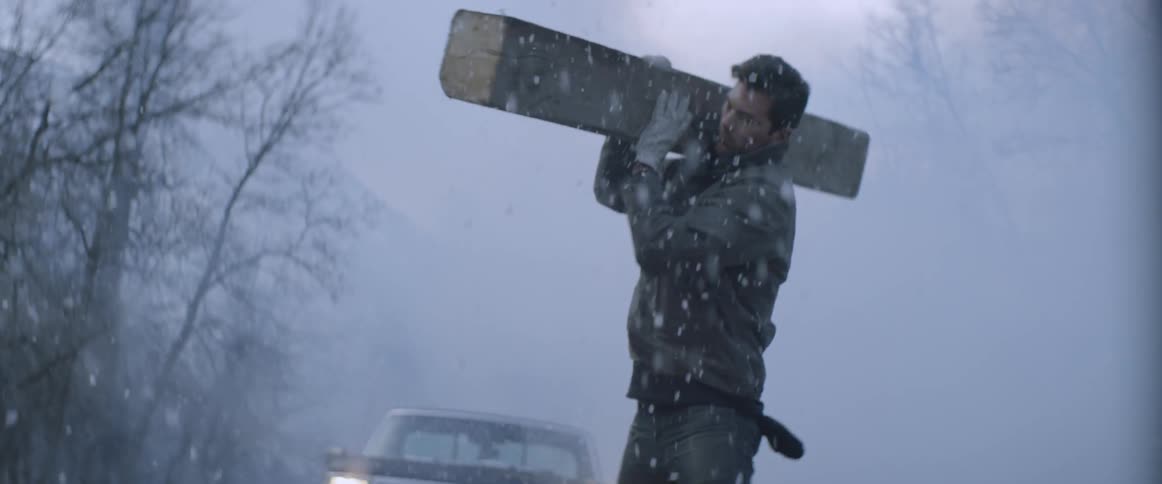 A man picks up a plank of wood in the snow
