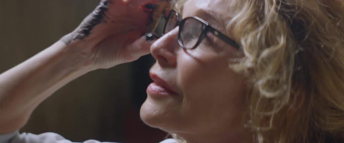 A woman adjusts her glasses with a paint-stained hand