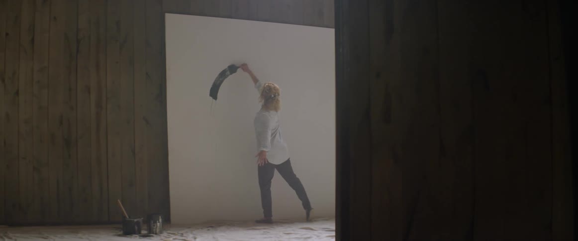 A female artist is using a paintbrush to put a stroke on a canvas