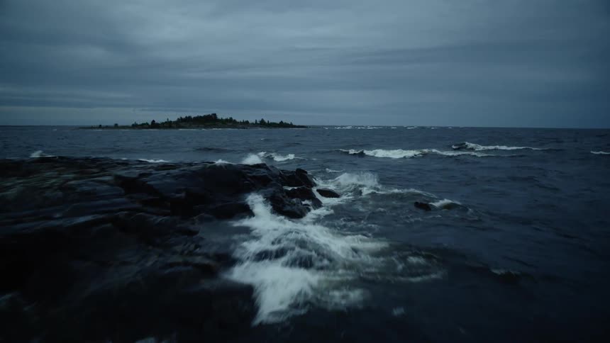 Waves are crashing over rocks in the ocean on a cloudy evening