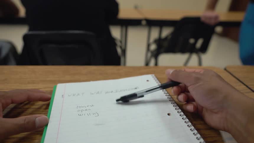 People sit as a man sits in a classroom giving a speech
