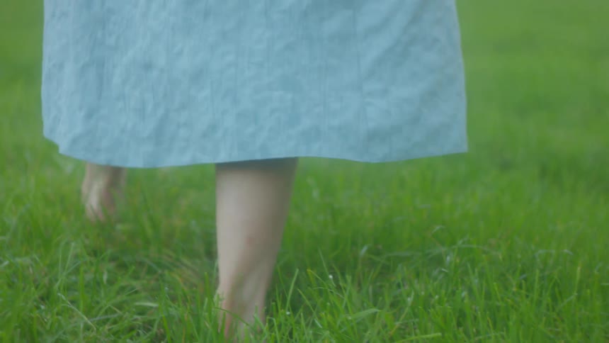 A girl in a dress is walking through grass with no shoes