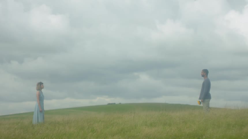A man and woman are standing in a field on a cloudy day staring at each other