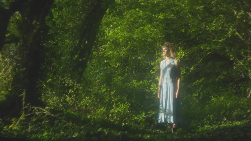 A woman stands in the green woods