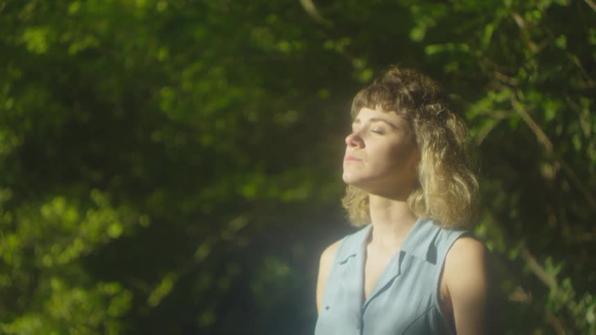 Woman stands alone in a forest with her eyes closed