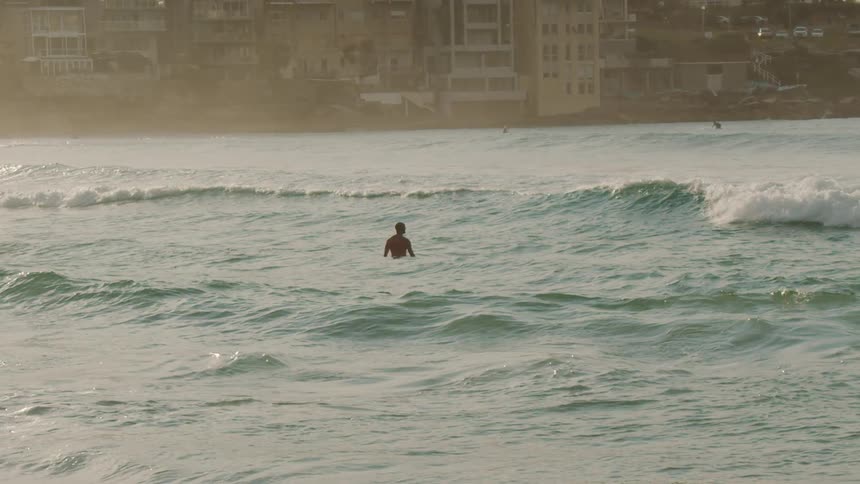 A person stands in the ocean as waves roll in