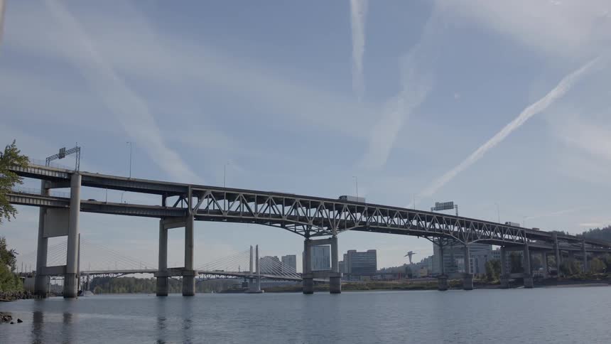 Vehicles are driving over a bridge leaving a city during the day