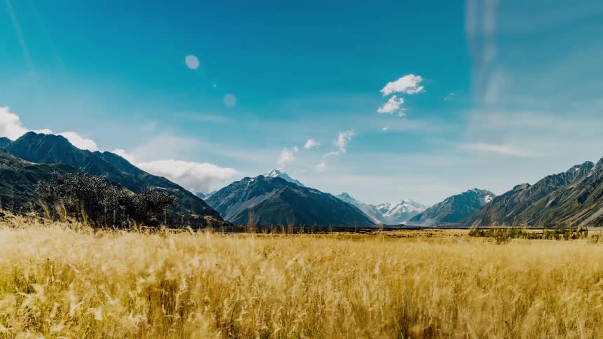 Grass blows in the wind as clouds move over mountain peaks