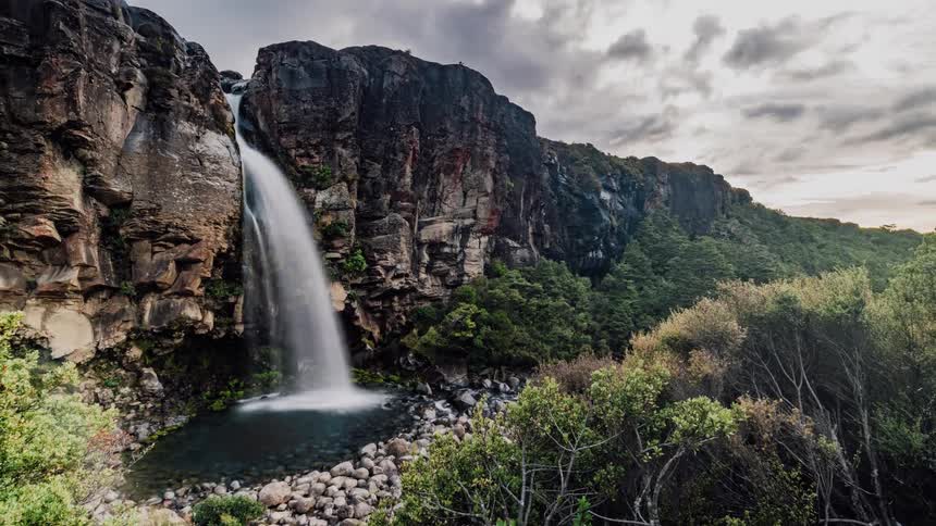 Waterfall pouring water from rock cliff in wilderness on cloudy day