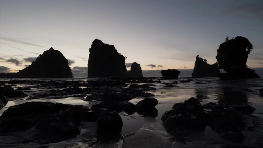 The tide rolls in over rocks on a beach at dusk