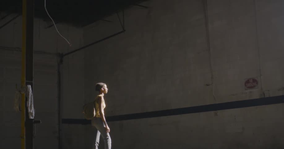 A woman carrying a backpack is standing inside an abandoned building during the day