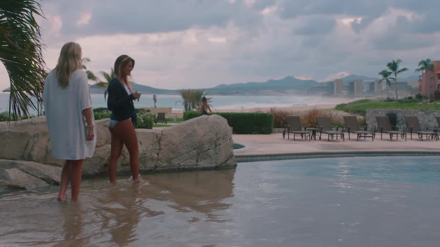 Women carrying drinks wade into a shallow pool