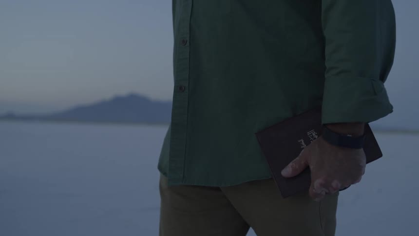 A man carrying a book walking on salt flats at sunset