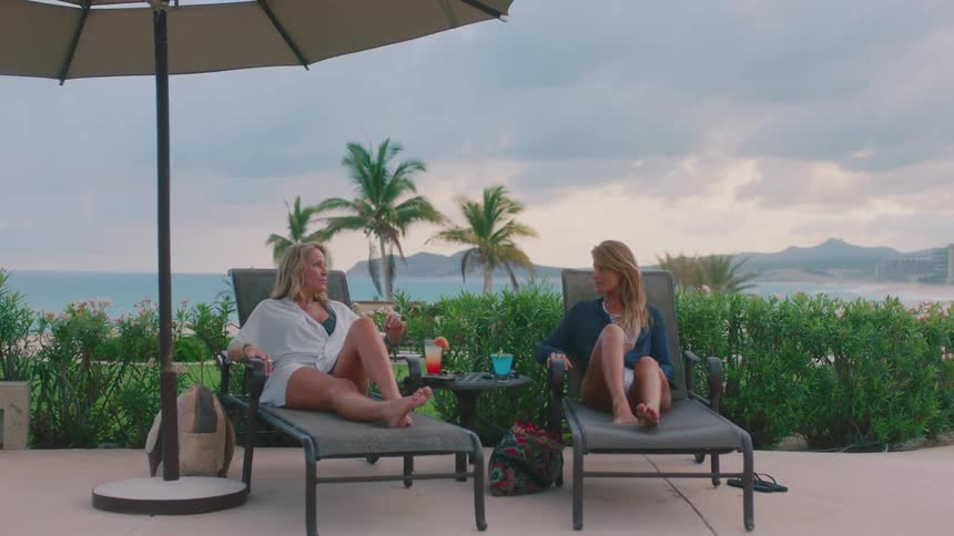 Two women are laying in chairs next to the beach