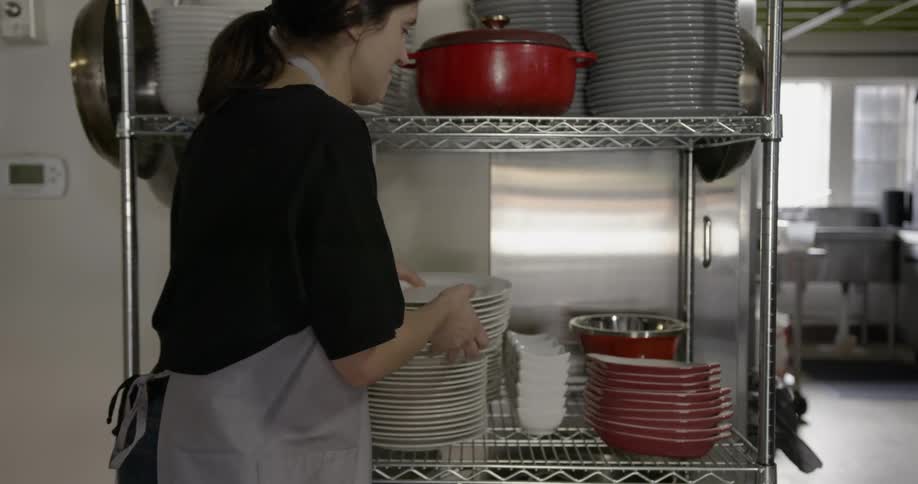 Woman takes some plates from stack of plates on metal rack shelf in kitchen