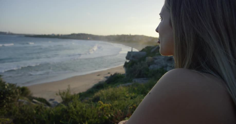 A woman sits on a cliff overlooking the beach and ocean
