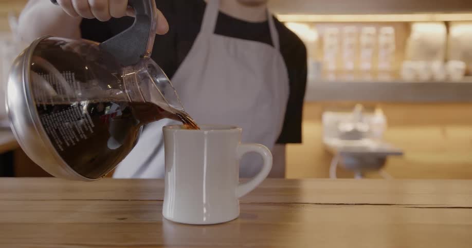 A worker pours coffee into a cup for another person