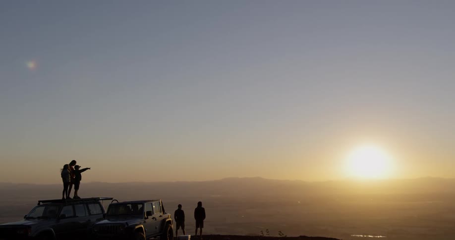 People watch a sunset while standing on a car roof