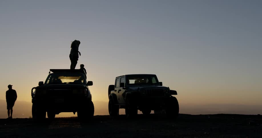 People are standing on top of an suv in a natural setting at dusk