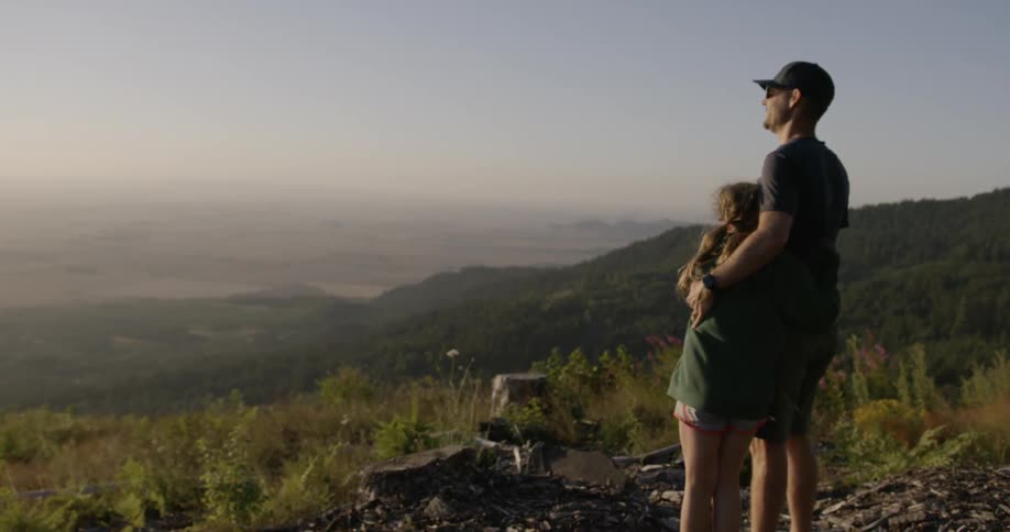 A father hugs his daughter while looking out over the mountains