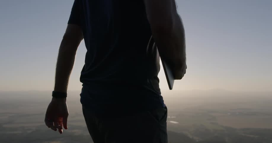 A man carrying a notebook walks along the top of a hill towards the sunshine