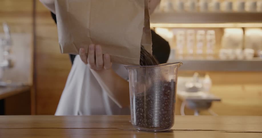 A woman pours coffee beans into a measuring cup