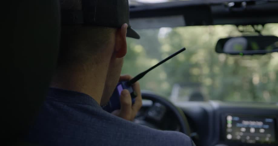 A man is talking on a walkie talkie as he drives during the day