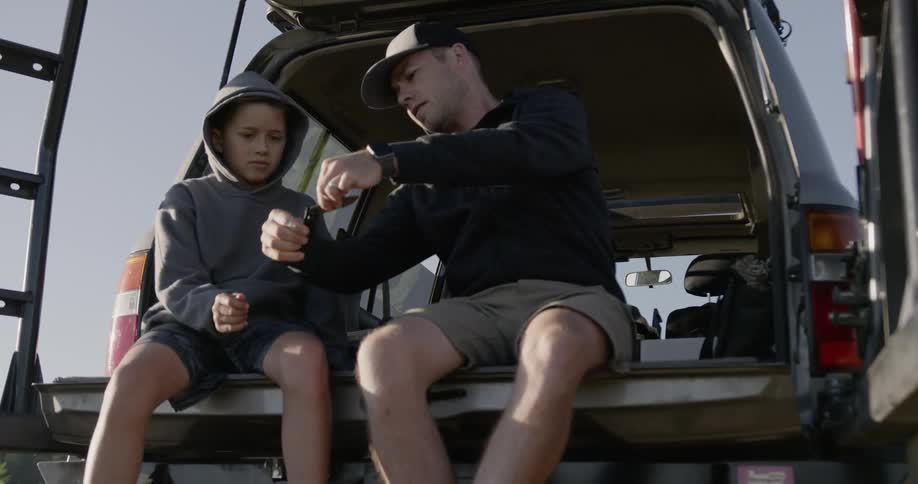 Man gives boy a pocket knife while sitting on a truck bed