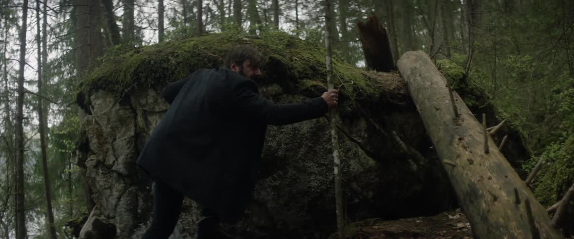A man is climbing up an incline in a forest during the day