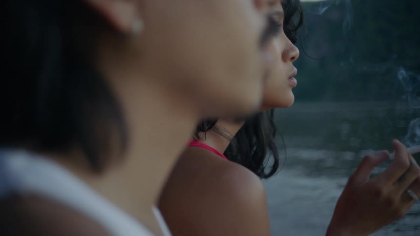 A man and woman sit by the water and smoke