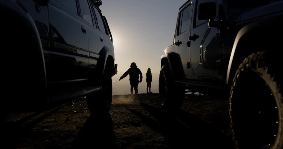 A boy jumps off a jeep and runs to a ridge at dusk