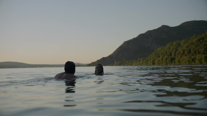Man and woman swim in a mountain lake at sunset