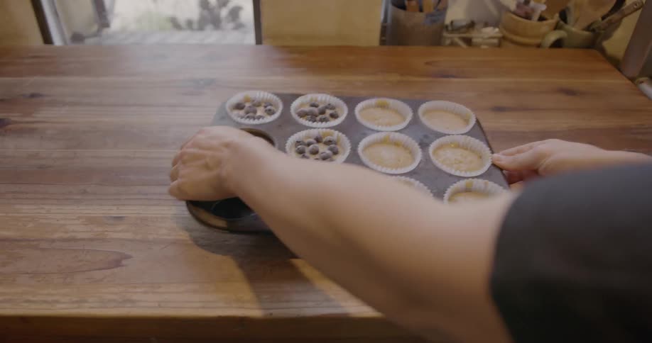 A person picks up a tray of raw muffins