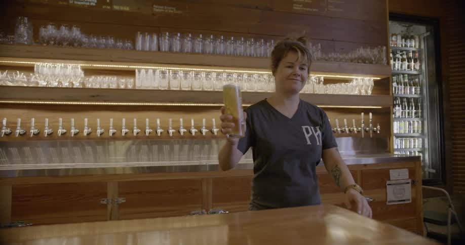 A woman in a taproom is pulling a draught of beer and serving it up
