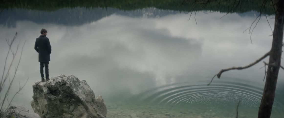 A man is standing on a rock in front of a lake