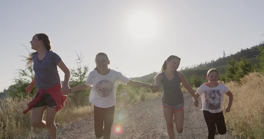 Four girls are holding hands and running through a field