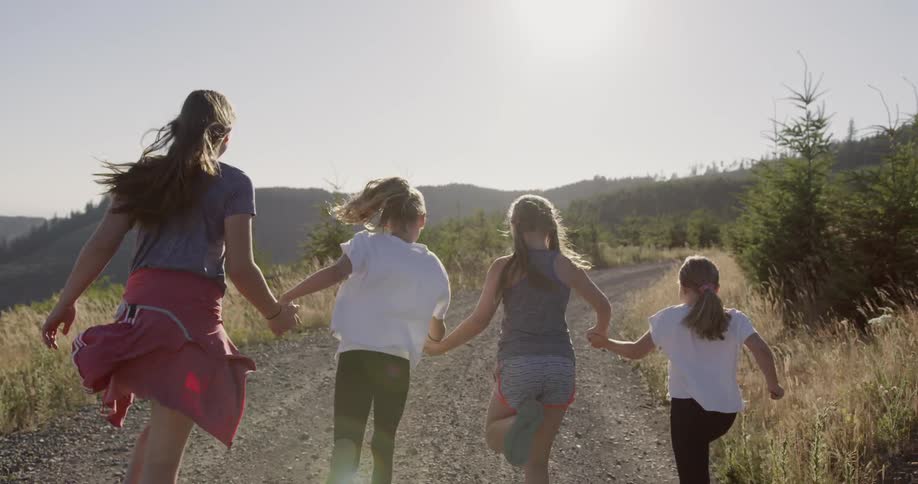 Four girls hold hands while running on a rocky path