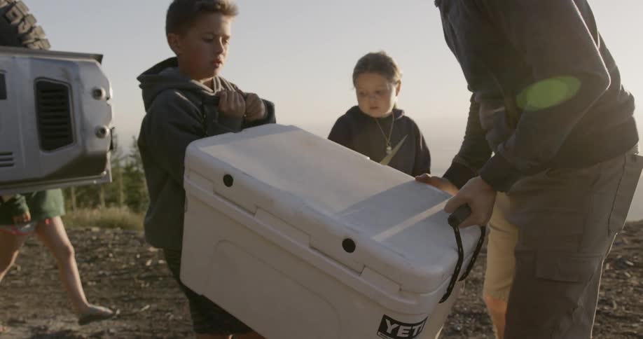 A man and a boy carry a cooler out of a truck and put it down