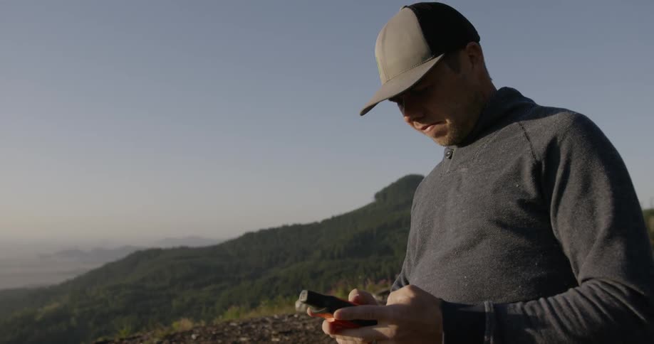 A man stands on a hilltop looking at GPS unit