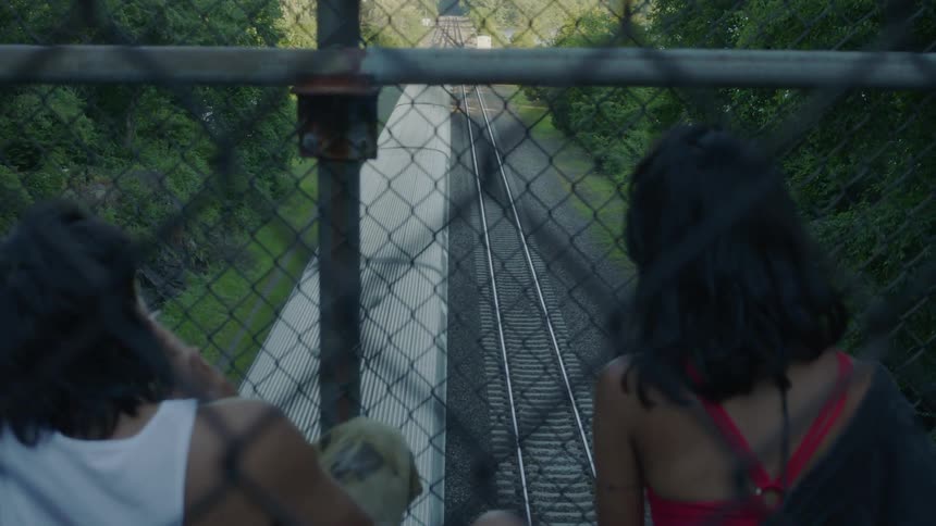 A man and woman are sitting on a bridge watching a train roll by