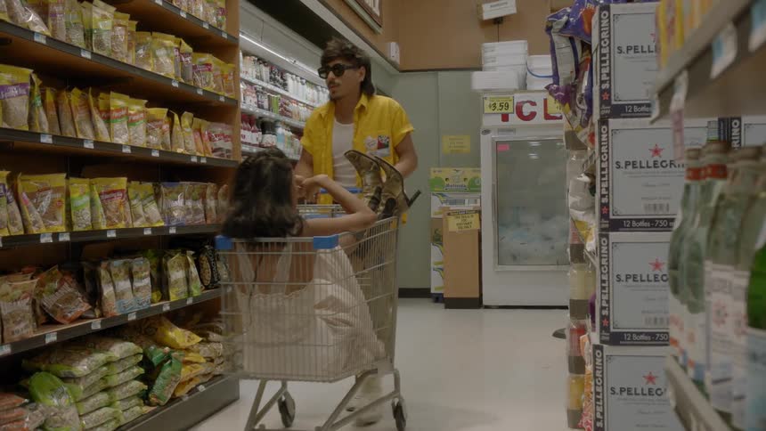 A man is pushing a woman in a cart down a supermarket aisle