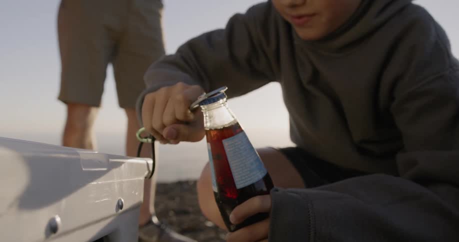A boy is opening a soda bottle outside during the day